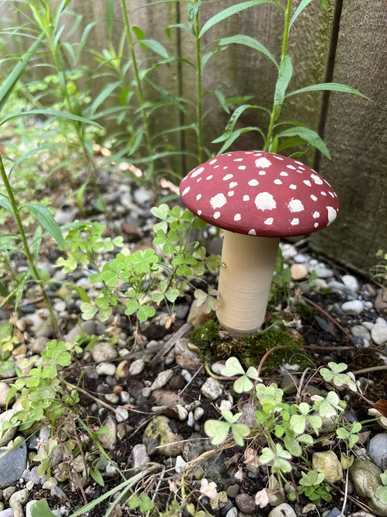 A red-and-white mushroom-shaped geocache container placed in a garden.